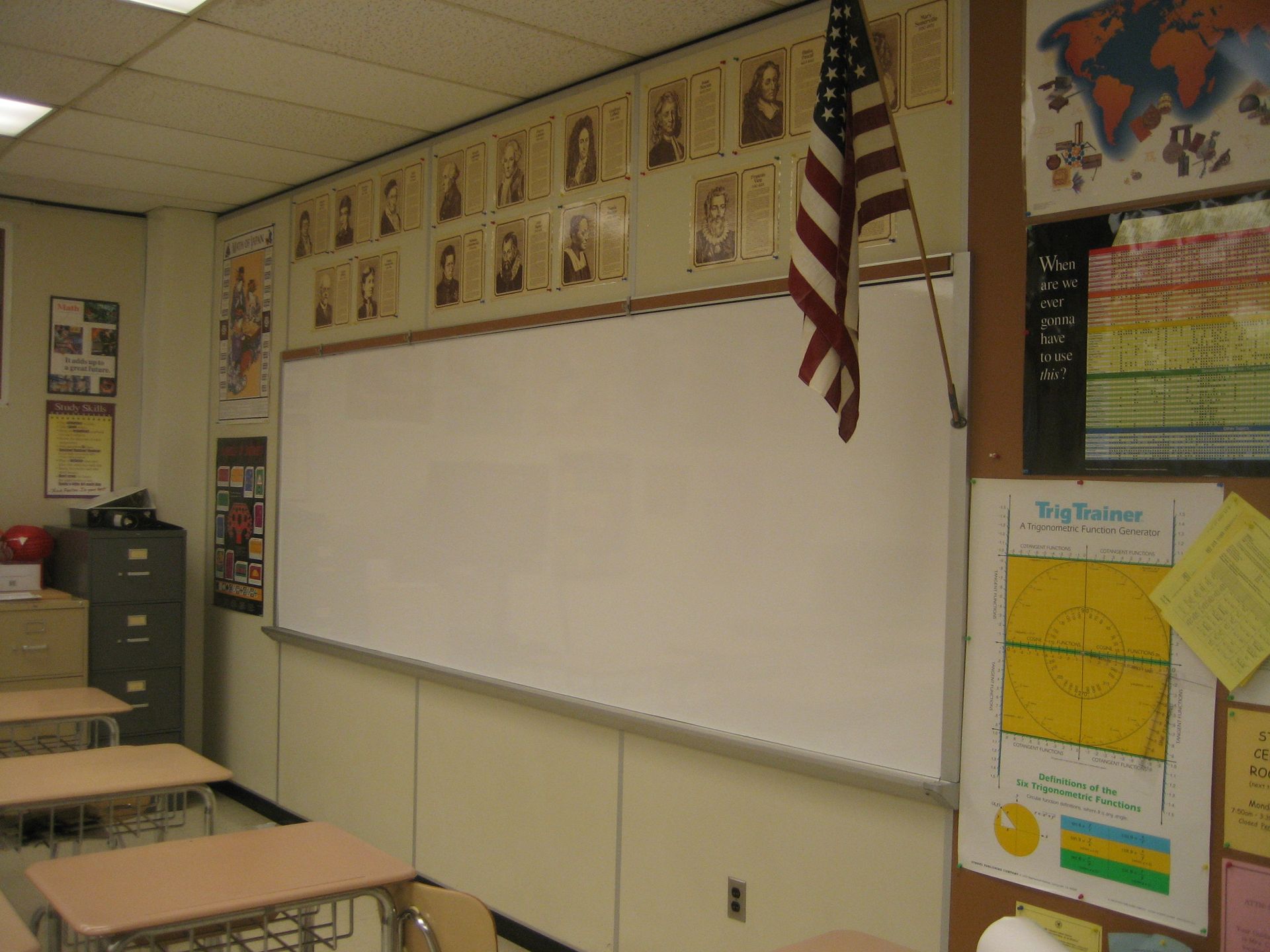 Empty classroom with whiteboard, desks, wall posters, and an American flag