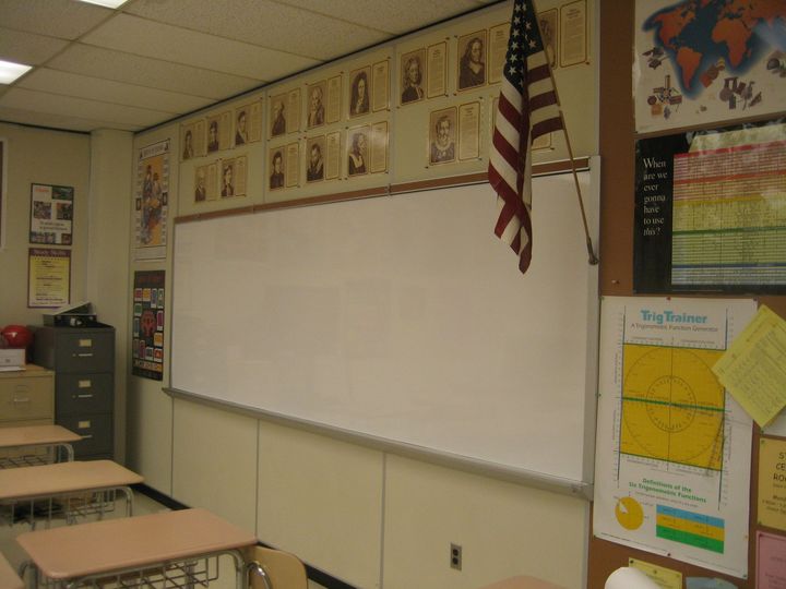 Classroom wall with large whiteboard, posters, desks, and an American flag hanging nearby