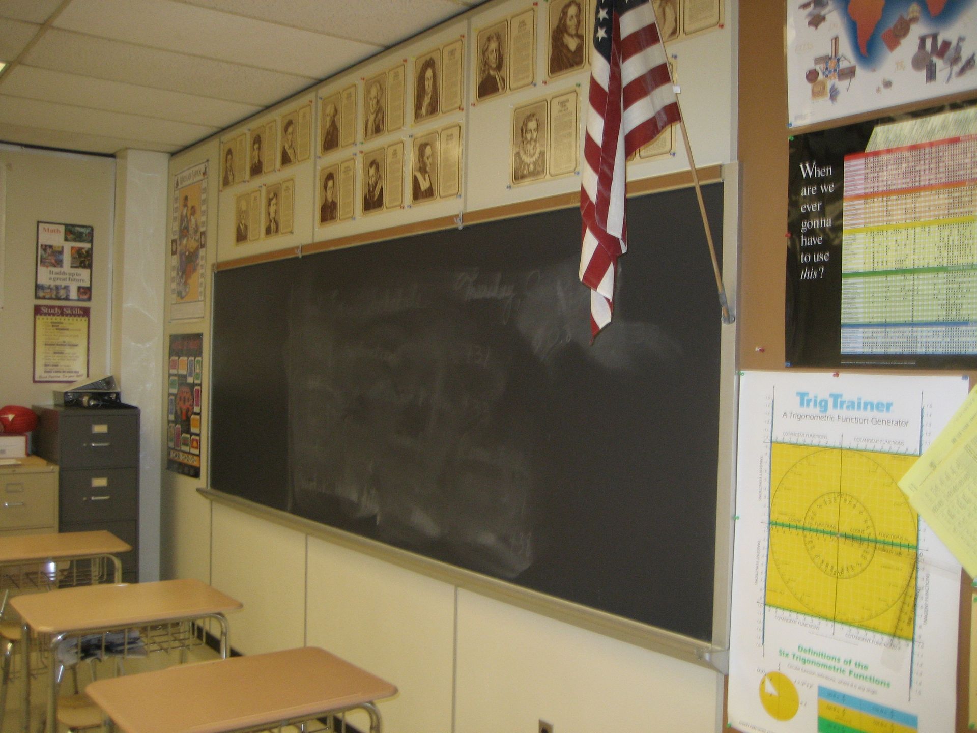 Empty classroom with a large blackboard, desks, and a hanging American flag.