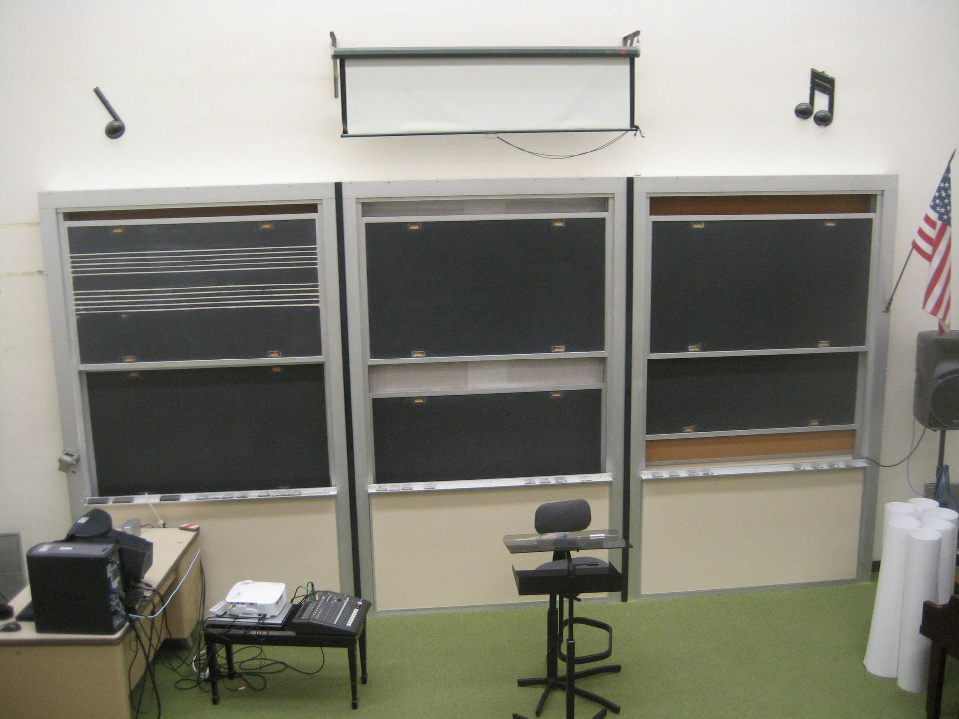 Empty classroom with three windows, a blackboard, music notes on the wall, and a stool by the center window