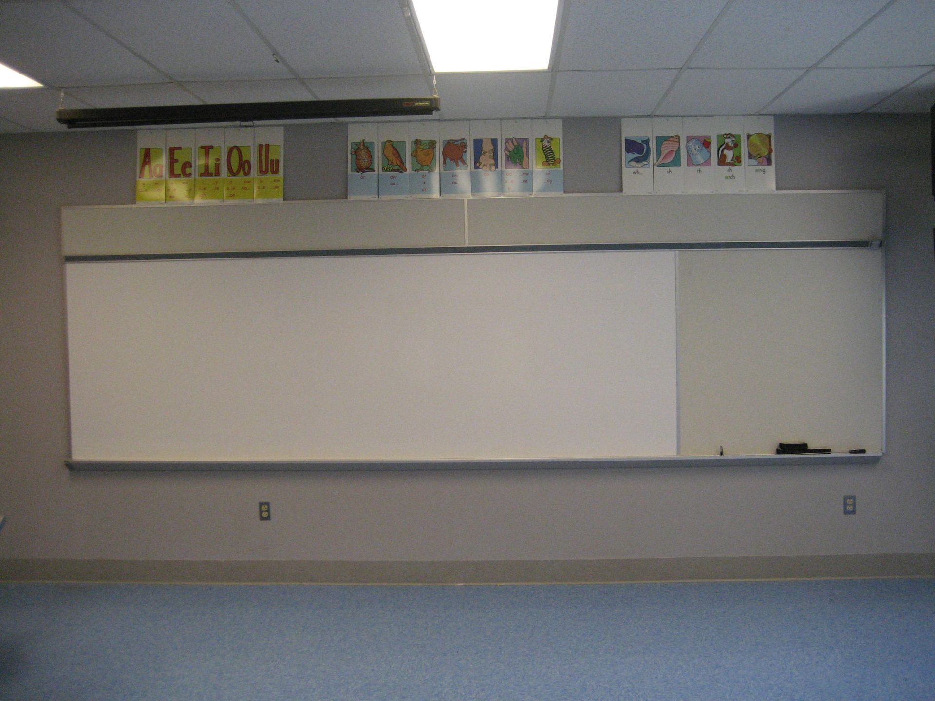Empty classroom with a large whiteboard, tiled ceiling, and posters above it.