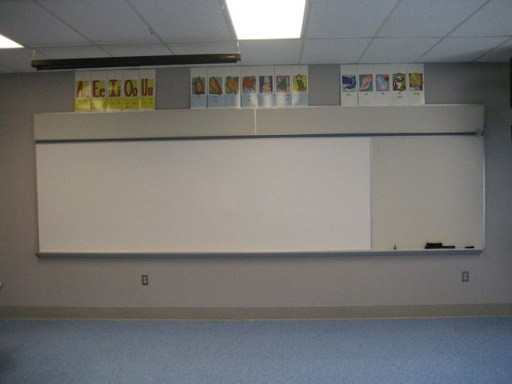 Empty classroom with a large whiteboard and colorful alphabet posters above it.
