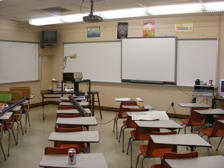 Empty classroom with rows of desks facing three whiteboards and a projector at the front.