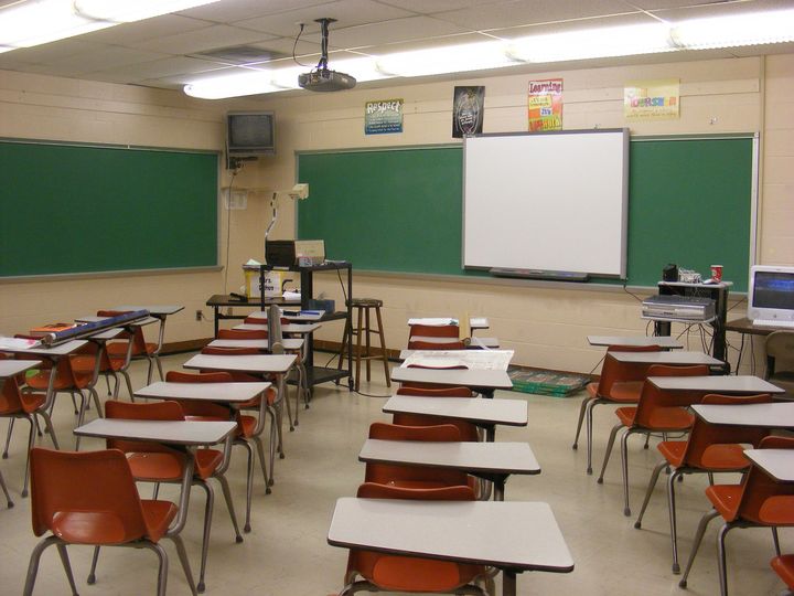 Empty classroom with desks, green chalkboards, and a white projection screen at the front.