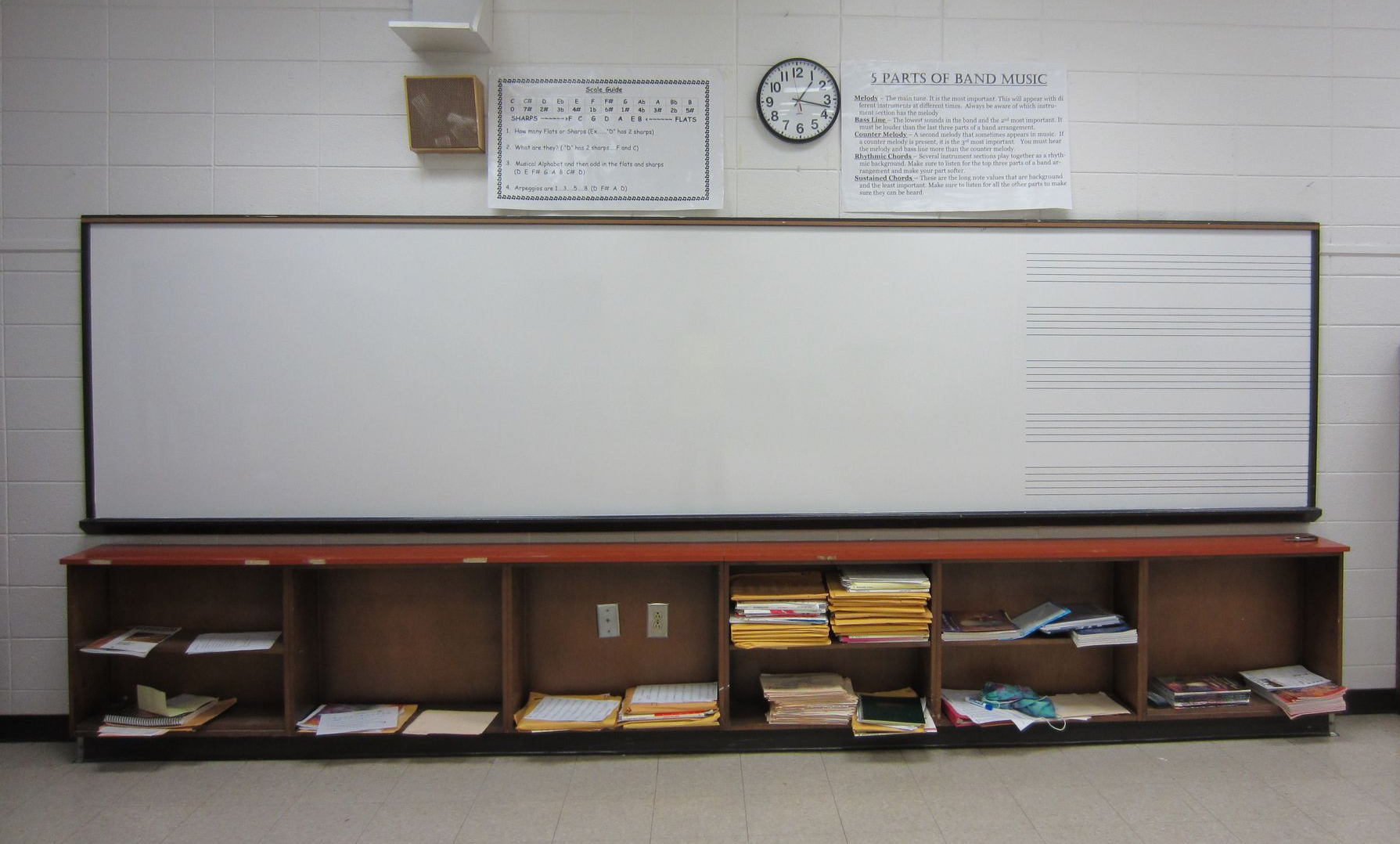 Classroom whiteboard with shelf and supplies, plus wall clock and calendar above.