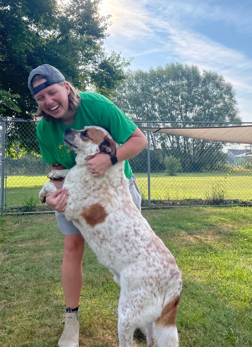 Person smiling and hugging a large spotted dog in a grassy yard.