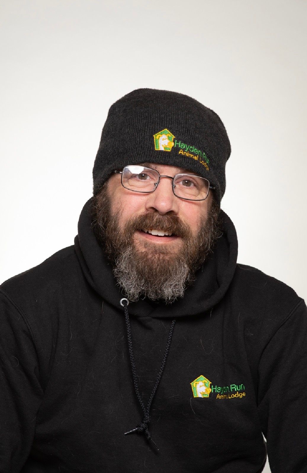 Woman with dark hair smiles, wearing a light blue sweatshirt, against a beige background.