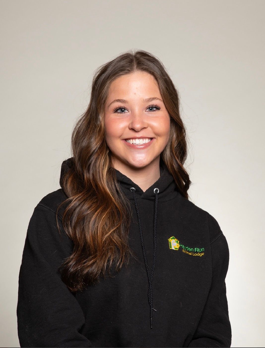 Woman with dark hair smiles, wearing a light blue sweatshirt, against a beige background.