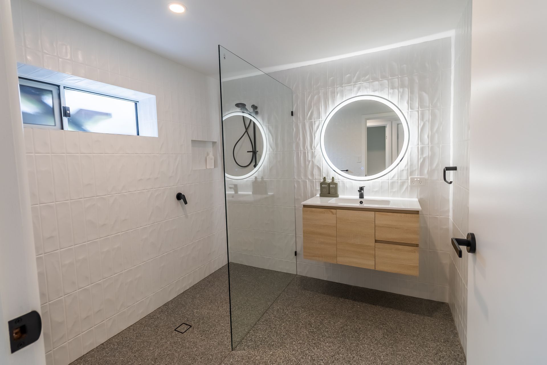 Modern bathroom with a floating wood vanity, round lighted mirrors, and a glass shower.