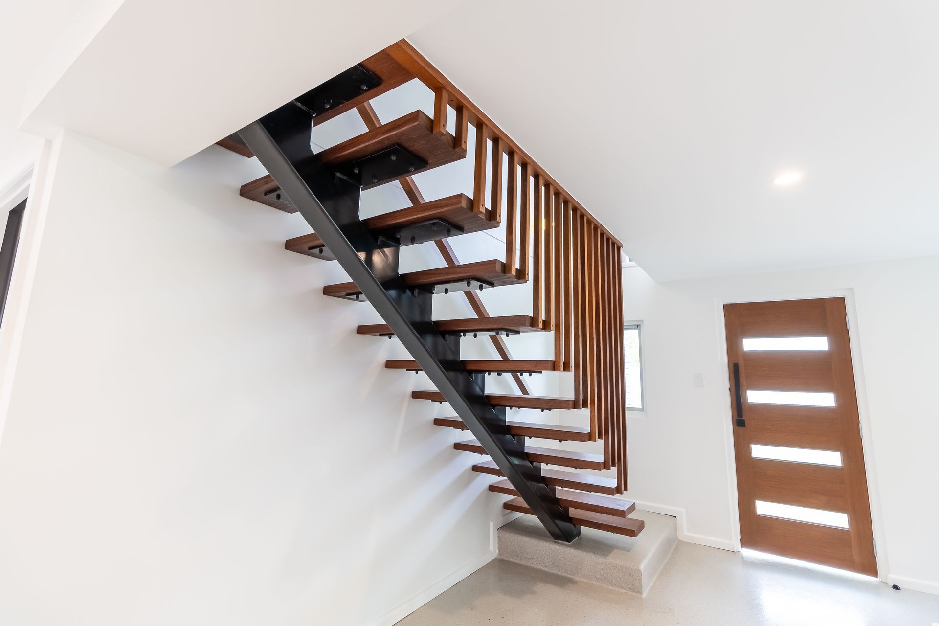 Wooden staircase with a metal support, leading up from a concrete step. Wooden door in the background.