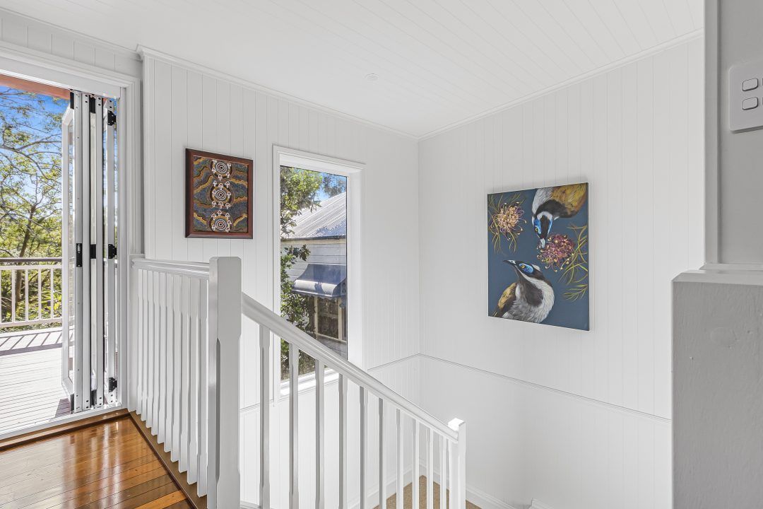 White interior with stairs, a painting, and a window overlooking greenery.