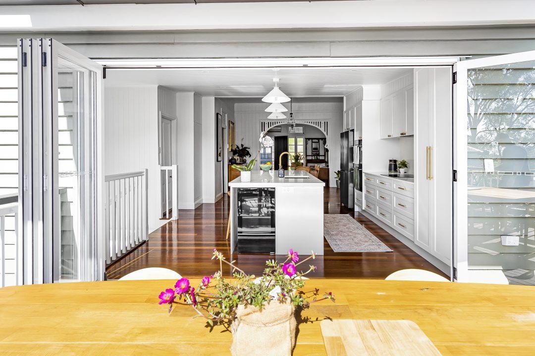 Kitchen with folding doors open to an outdoor dining area, featuring white cabinetry and a wooden table with flowers.