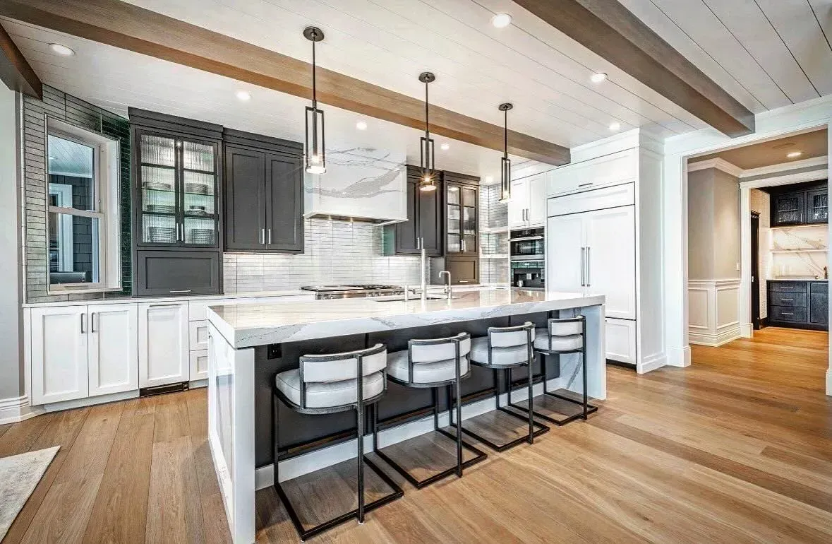 Modern kitchen with island seating, gray and white cabinets, and wooden floors.