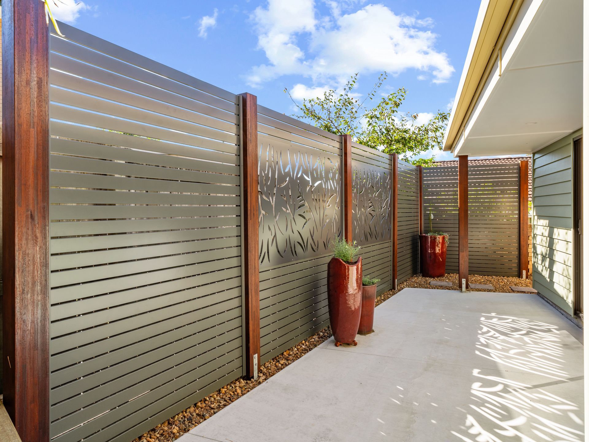 A modern outdoor fence with brown wood posts and dark gray metal panels, decorated with a decorative cut-out pattern.