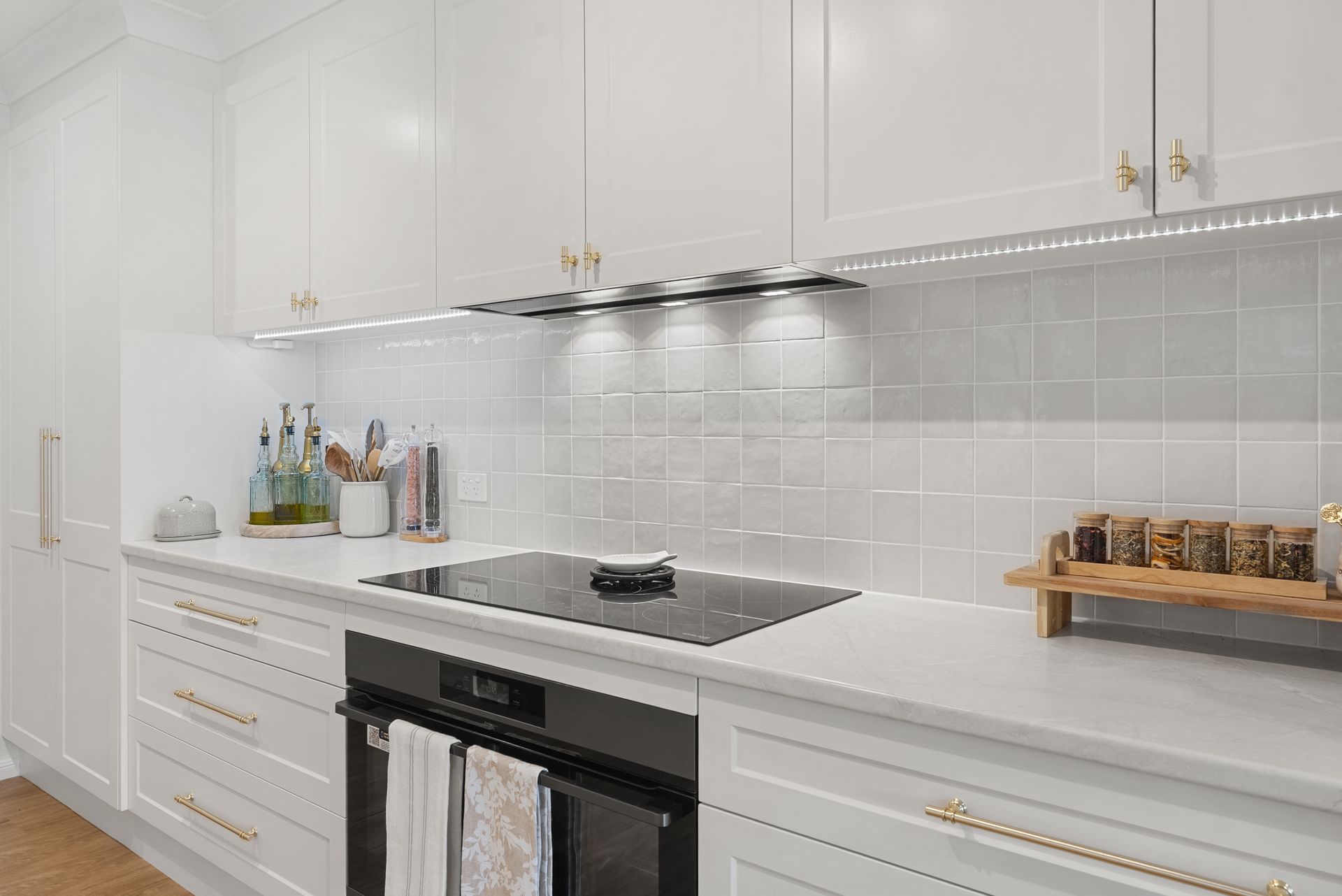White kitchen with cabinets, cooktop, oven, and tiled backsplash.