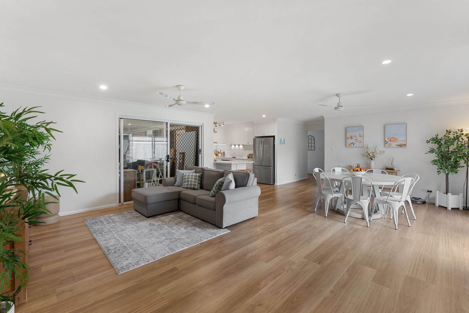 Open-plan living area with gray sectional, dining table, light wood floor, and white walls.
