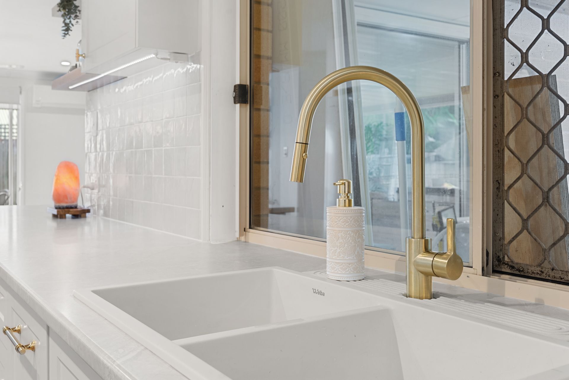 Gold faucet over a white double sink in a bright kitchen with white countertops.