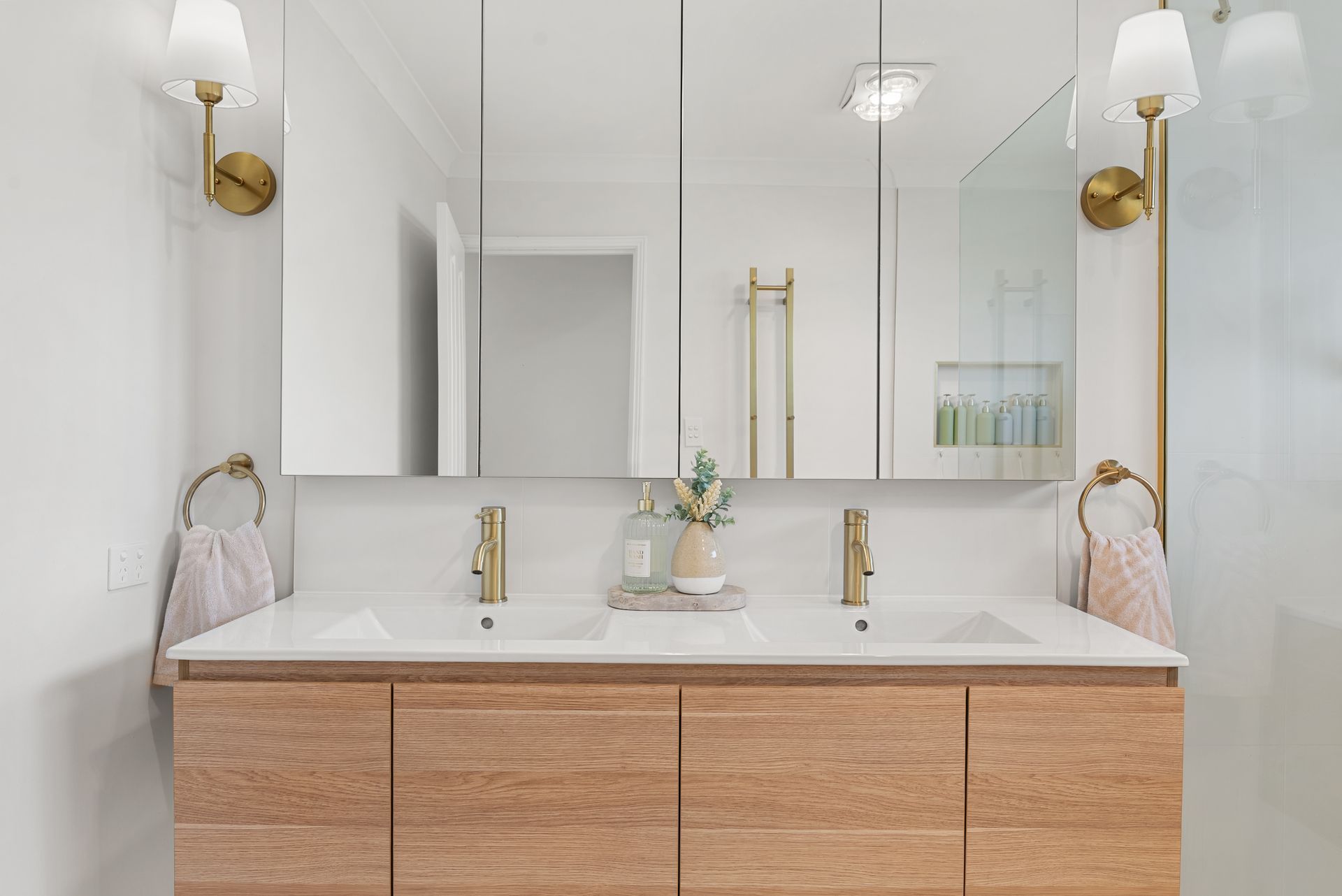 Bathroom with wood vanity, double sinks, gold fixtures, and mirrored medicine cabinets.