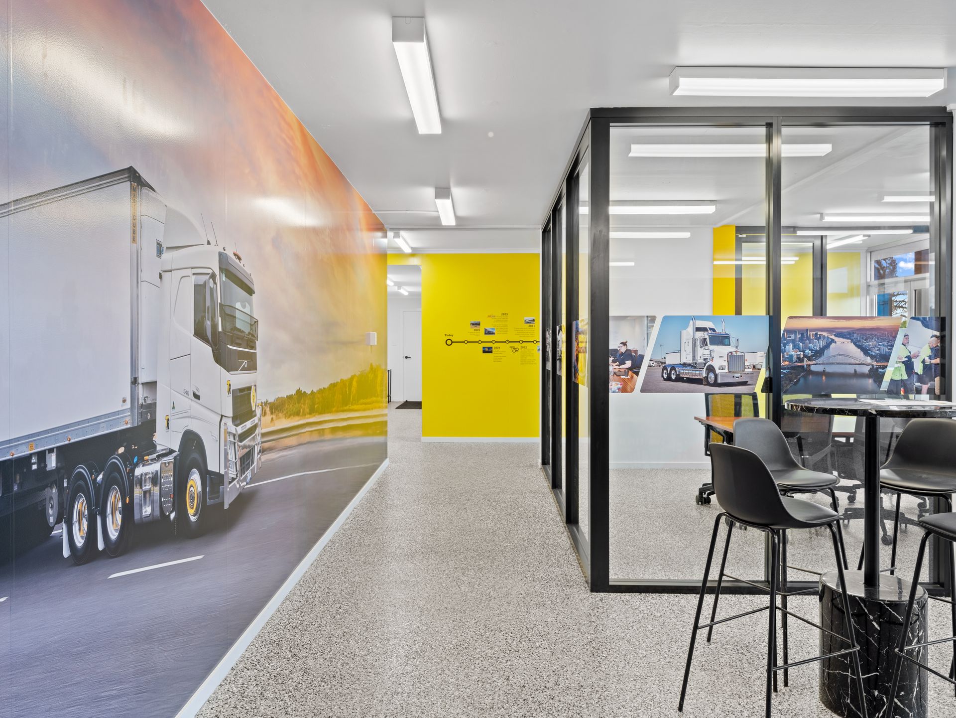 Office hallway with truck mural, yellow wall, glass doors, and seating area.