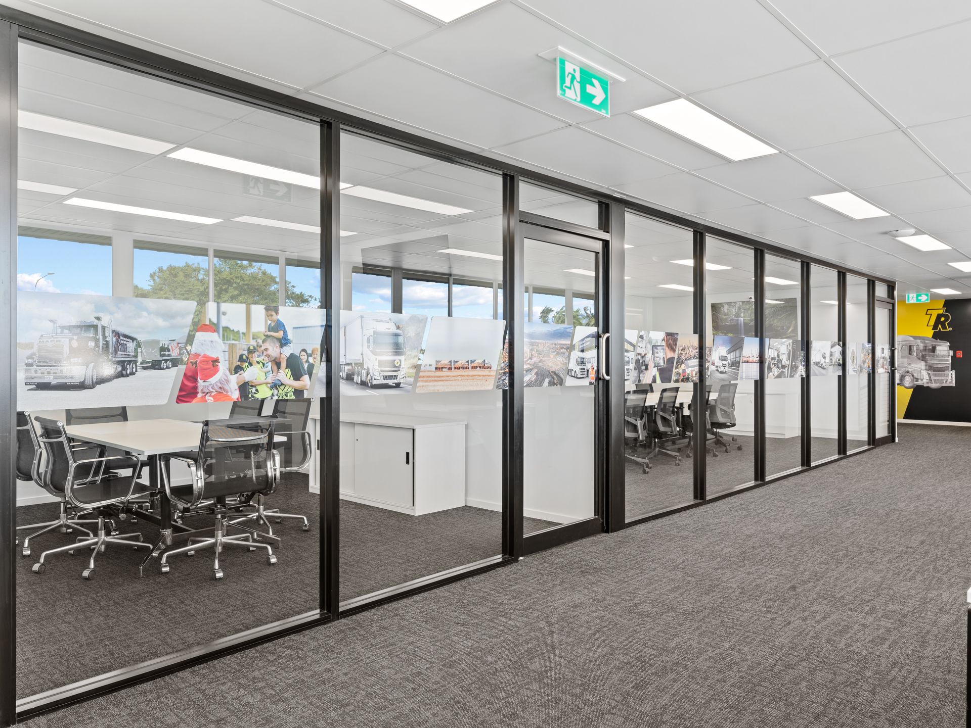 Office interior with glass walls, a conference table, and desks; a gray carpeted floor.