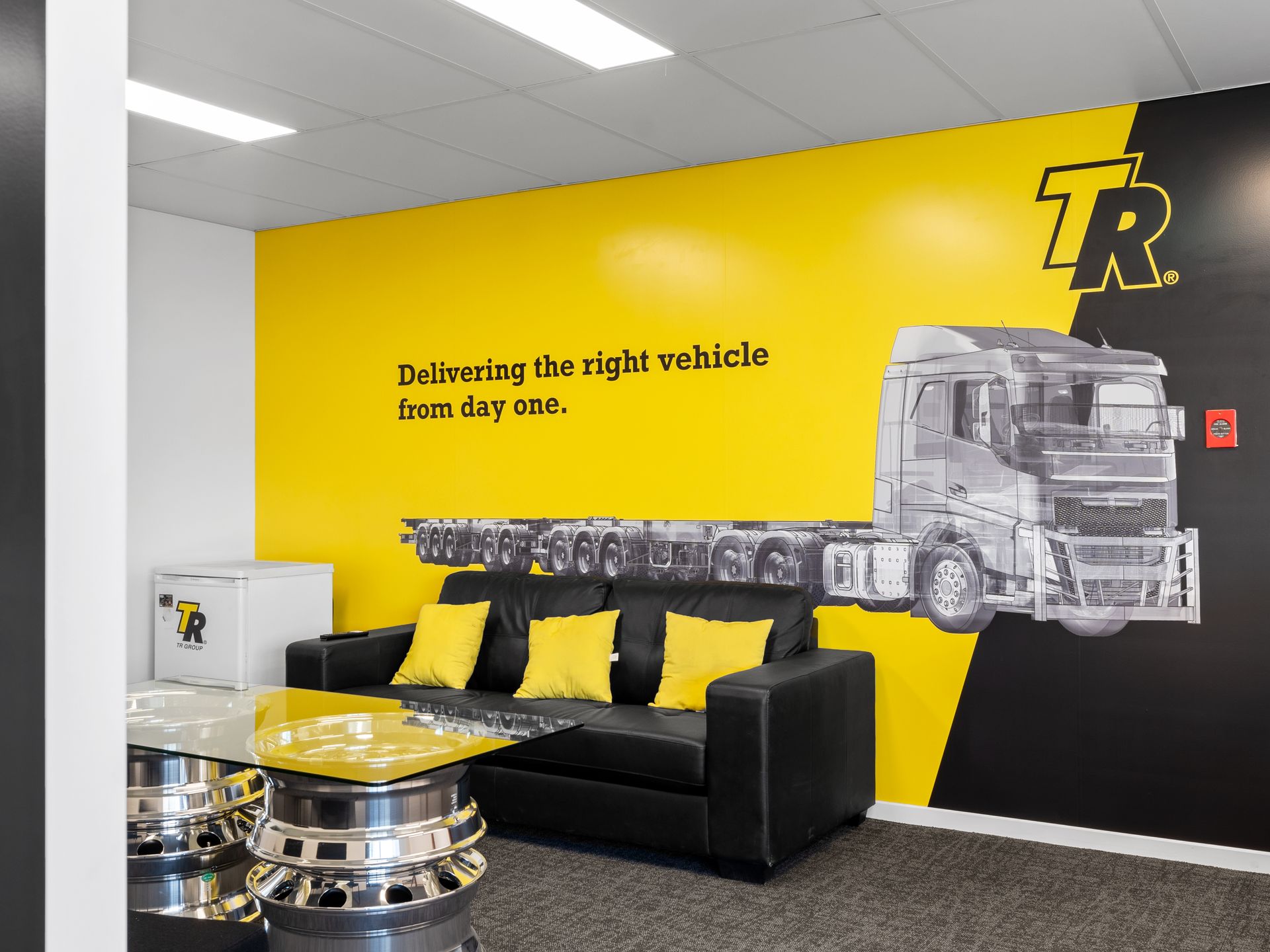 Office with yellow and black wall with logo, sofa, and truck graphic.