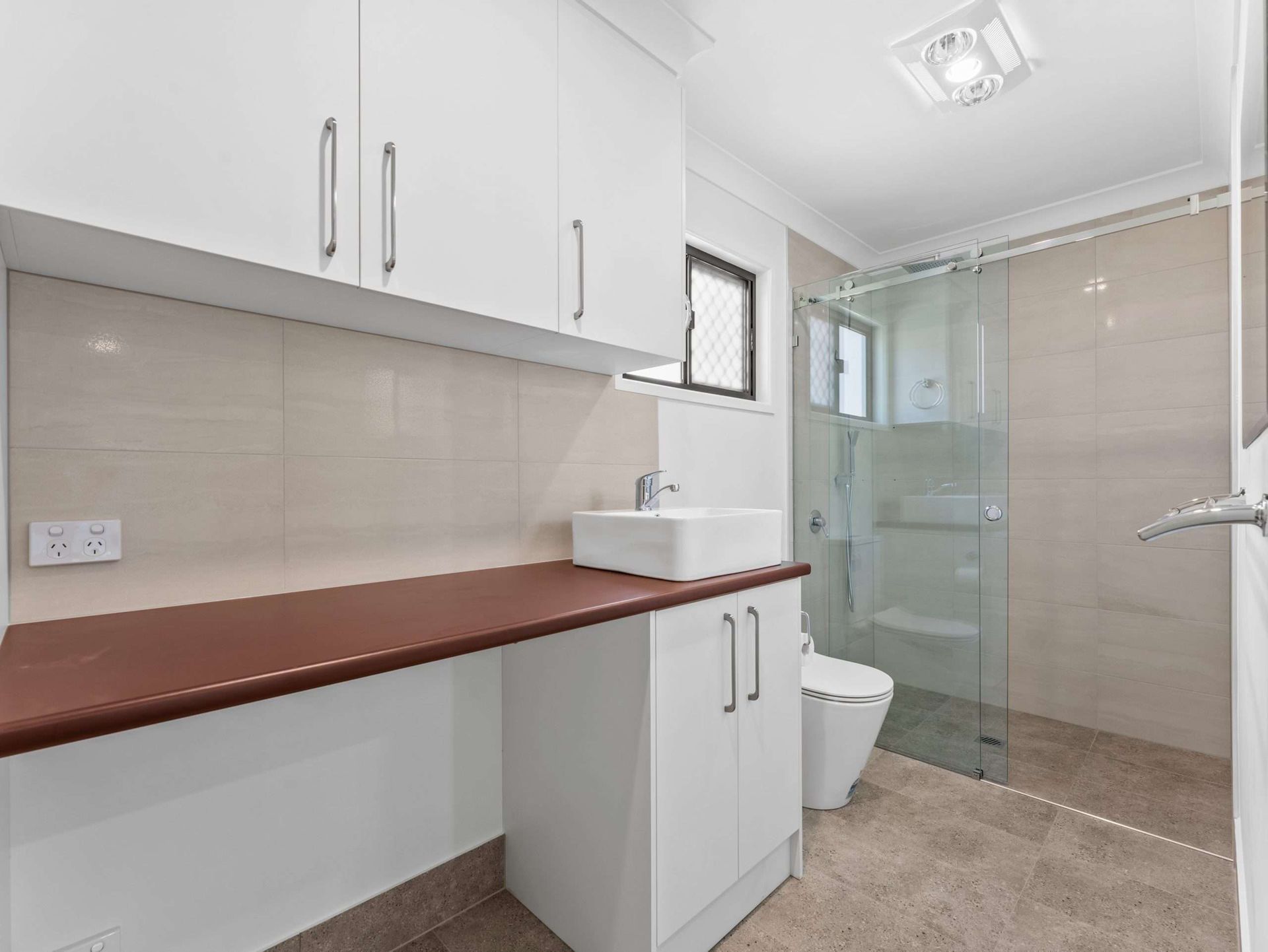 Bathroom with white cabinets, brown countertop, glass shower, and white toilet.