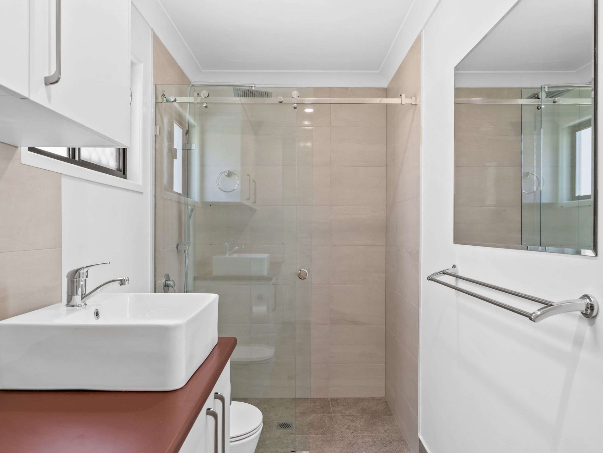 Bathroom with glass shower, white sink, brown countertop, toilet, and mirror.