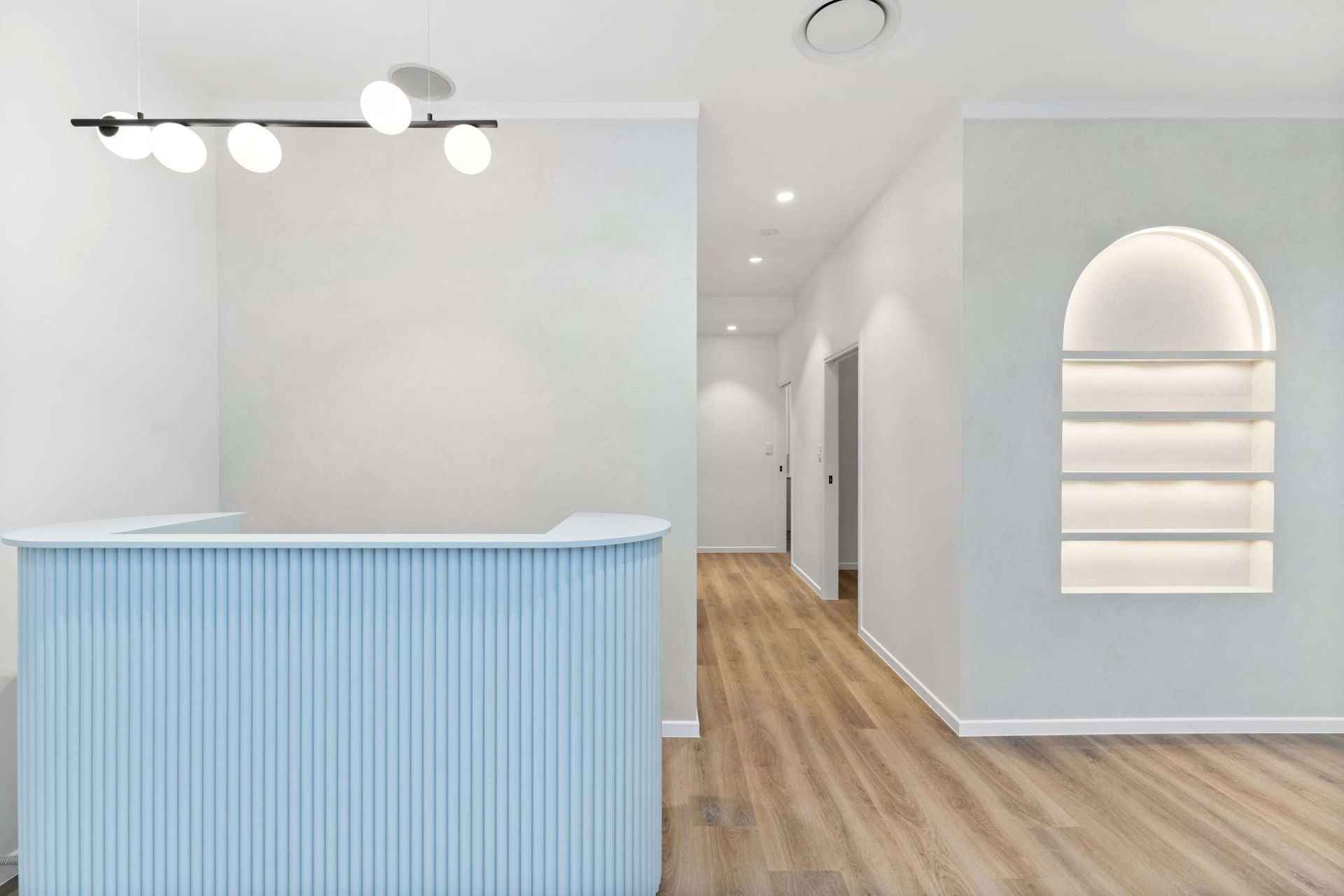 Reception area with blue desk, arched shelving, and hallway with wood floor.