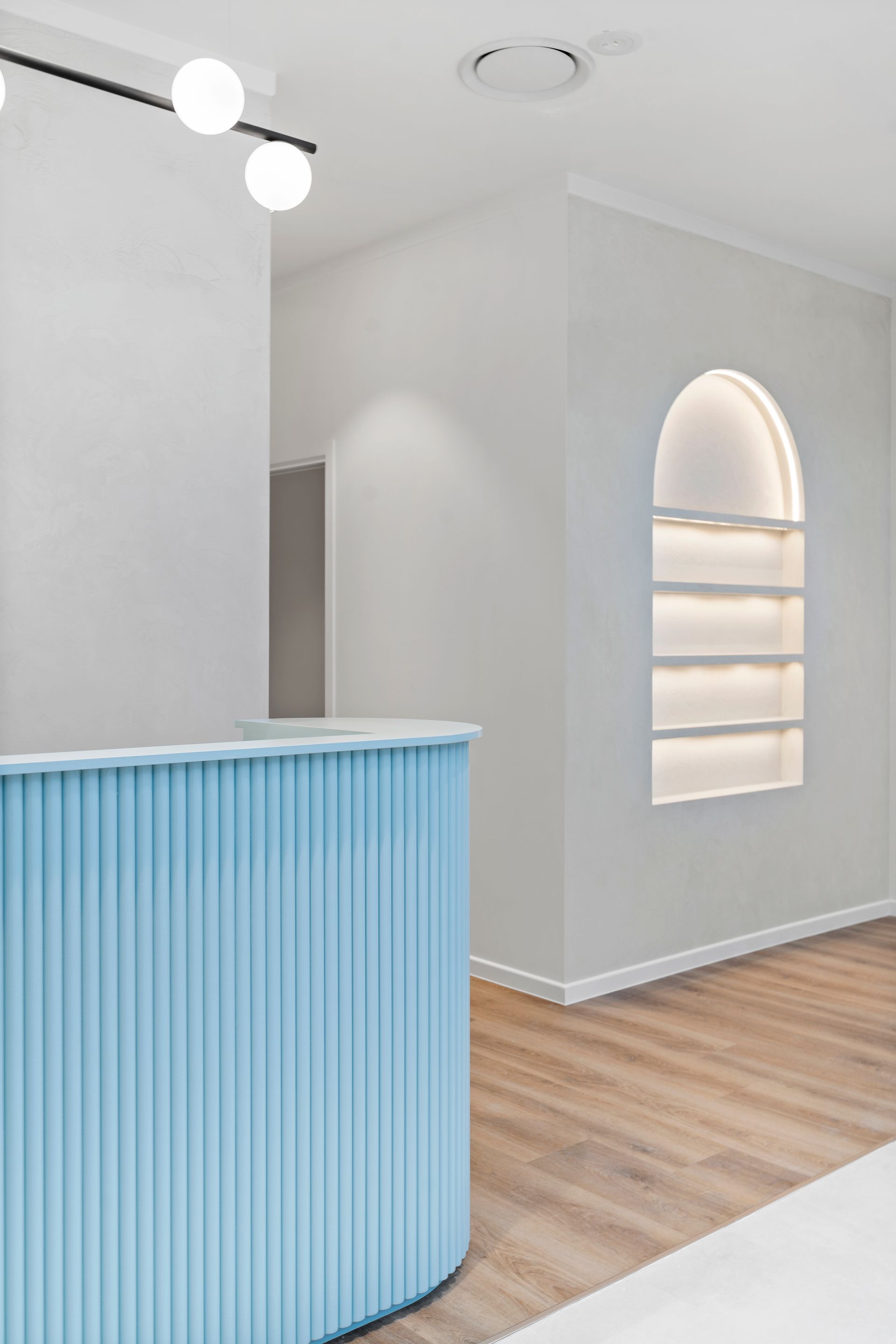 Blue reception desk in a white room with a wood floor and arched display case.