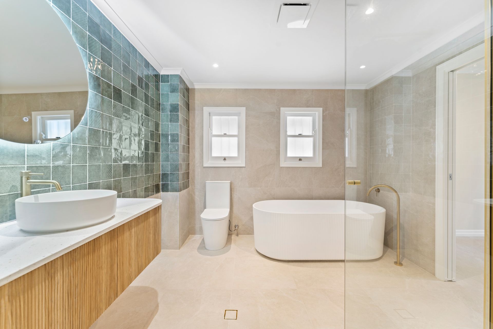 Spacious bathroom with a white tub, toilet, and sink; features teal tile wall and wooden vanity.