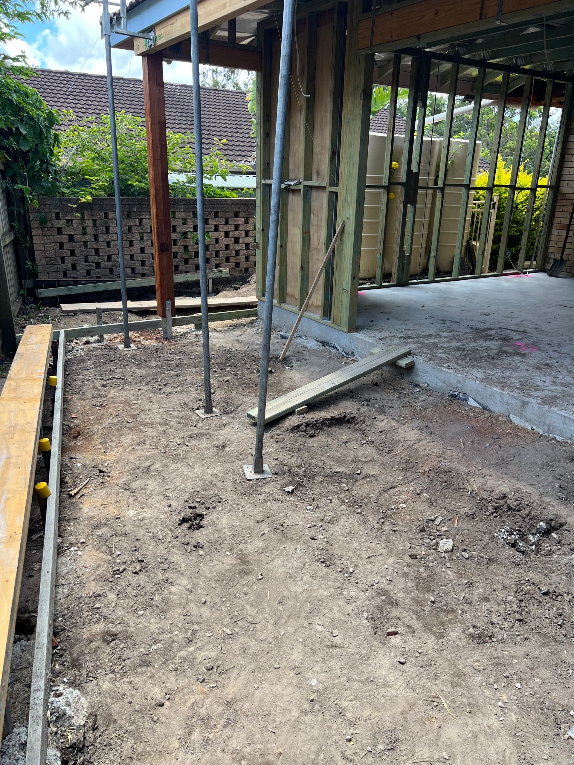 Construction site with dirt ground, wooden frames, metal support poles, and a brick wall.