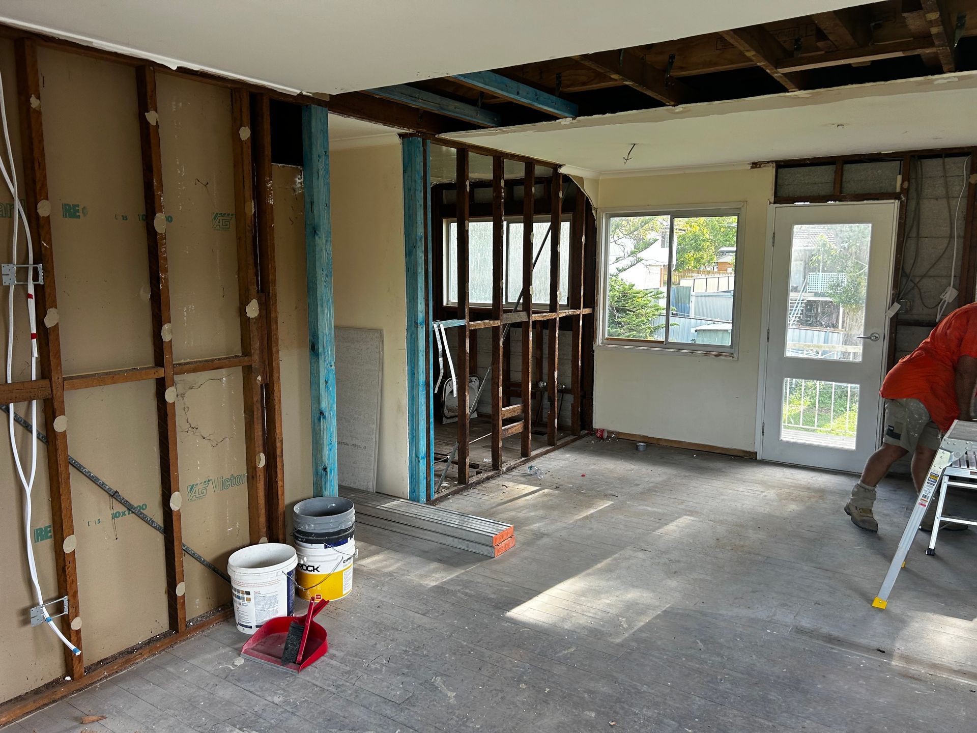 Interior room under renovation, exposed studs, open ceiling, window, door, person working.