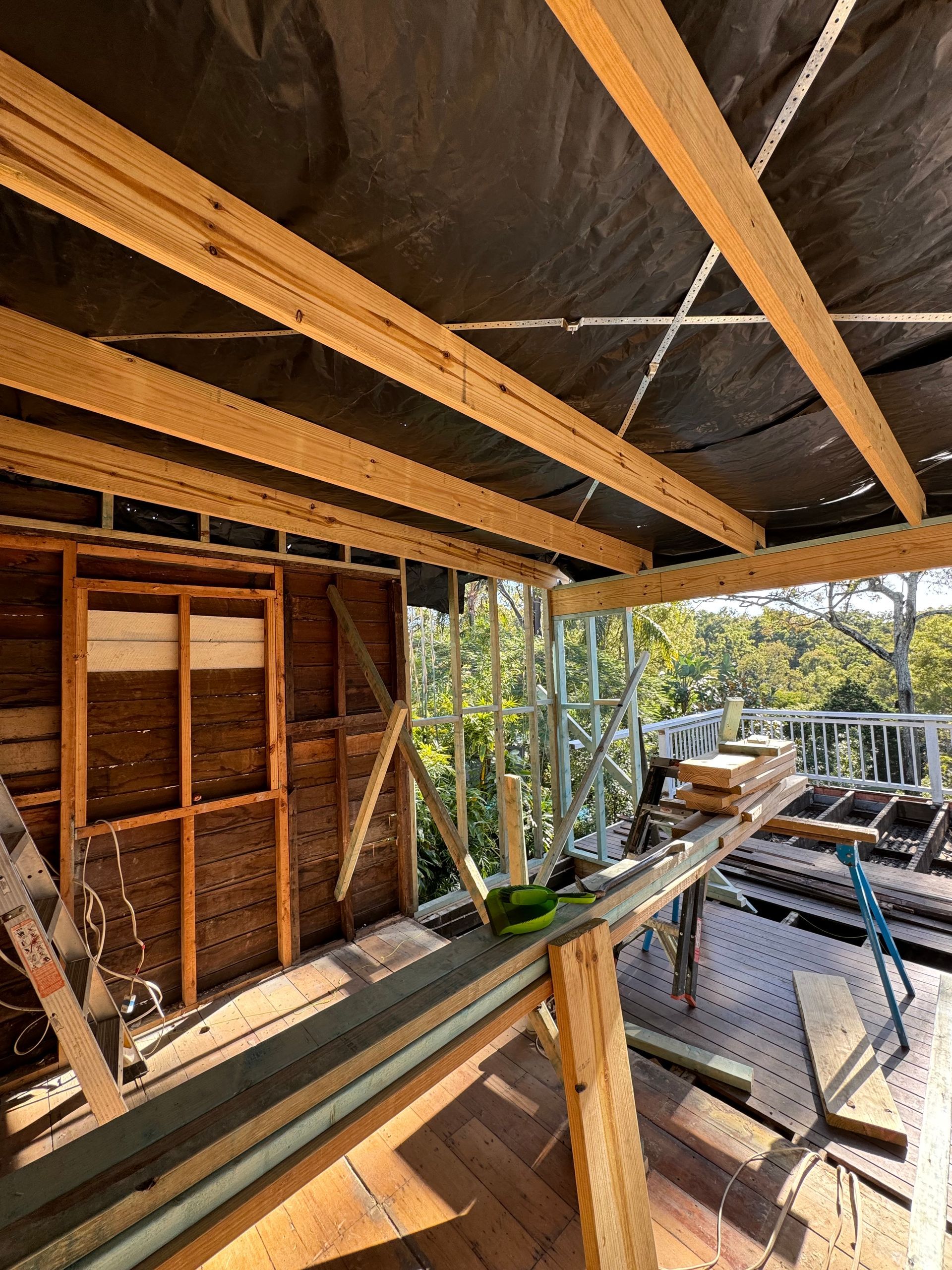 Construction site: wooden beams forming a roof structure.  A half-built deck with views of trees.