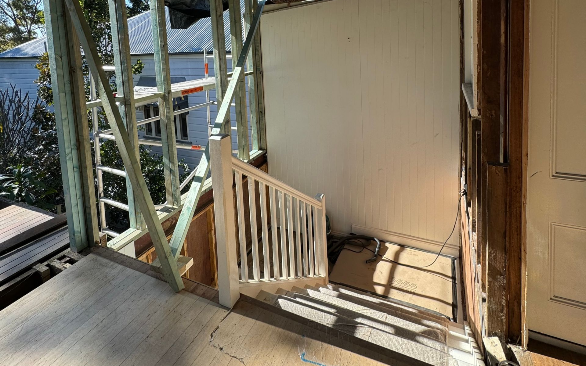 Wooden stairs with white railing, partially constructed structure, bright sunlight.