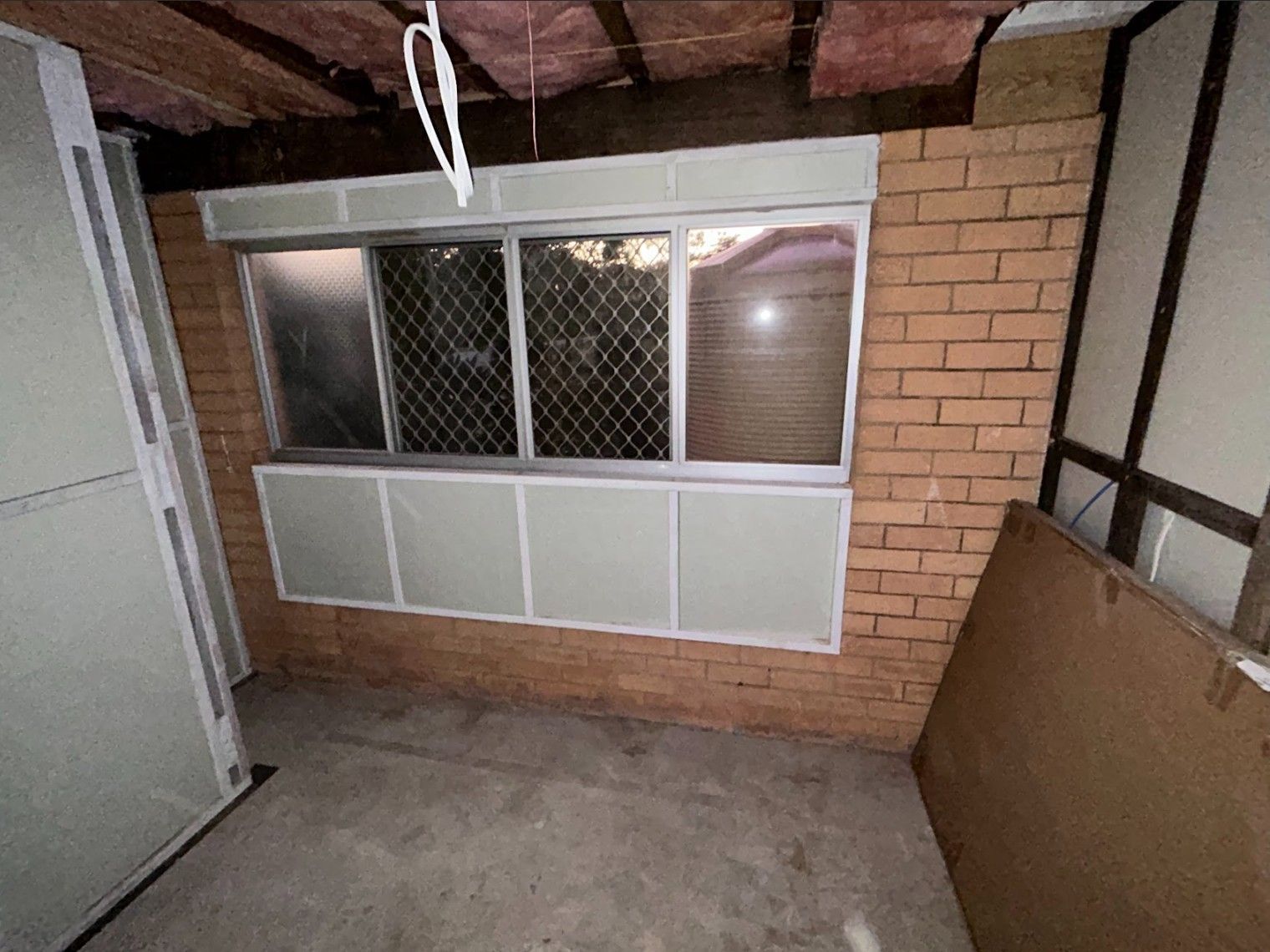 Window in a room with brick wall. Includes an air-conditioning unit and a cardboard panel.