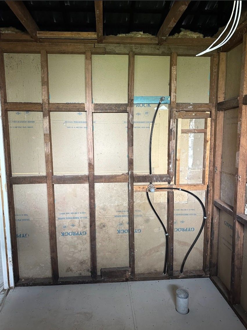 Interior wall framing with insulation, plumbing, and open ceiling.