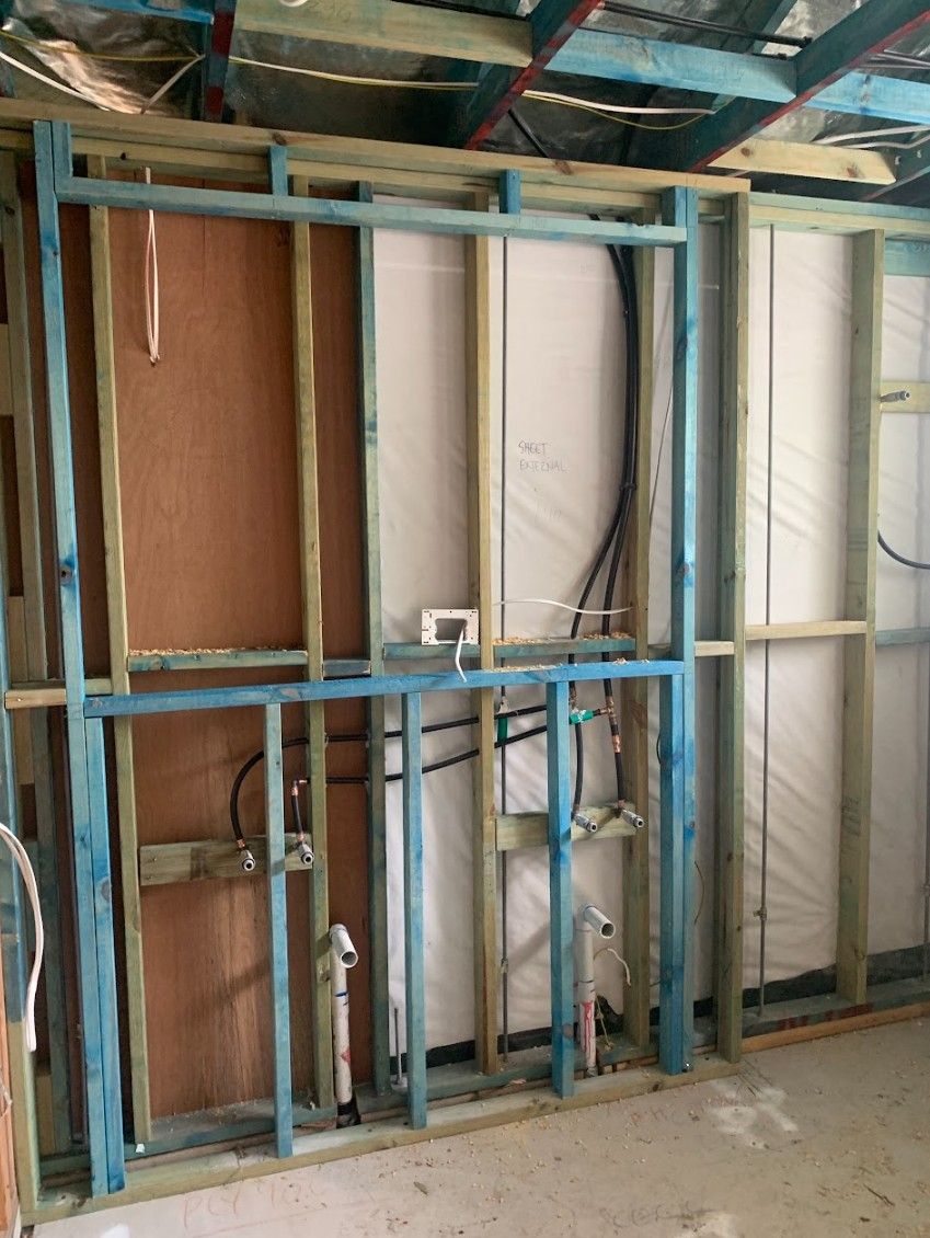 Interior wall frame with exposed plumbing and electrical wiring. Blue framing, white insulation, brown wood.