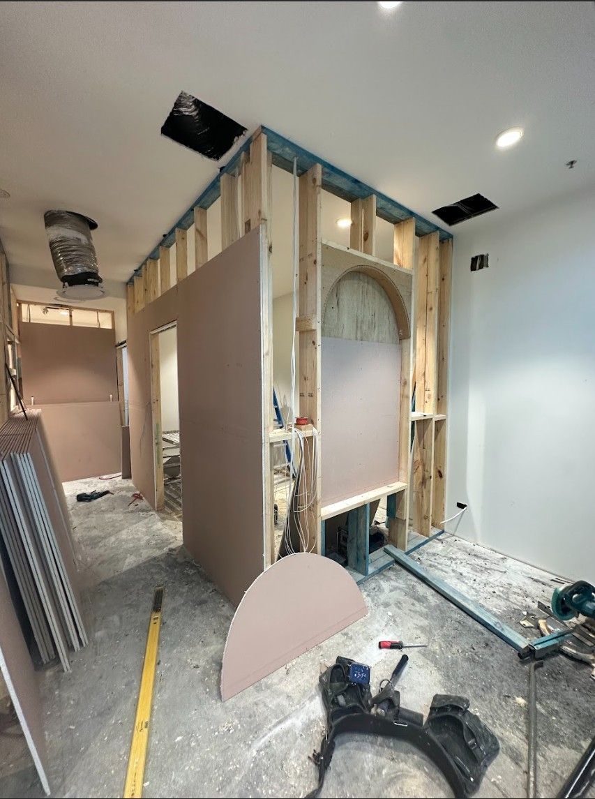 Construction of interior walls and ceiling, drywall and wooden studs visible, tools and materials on the floor.