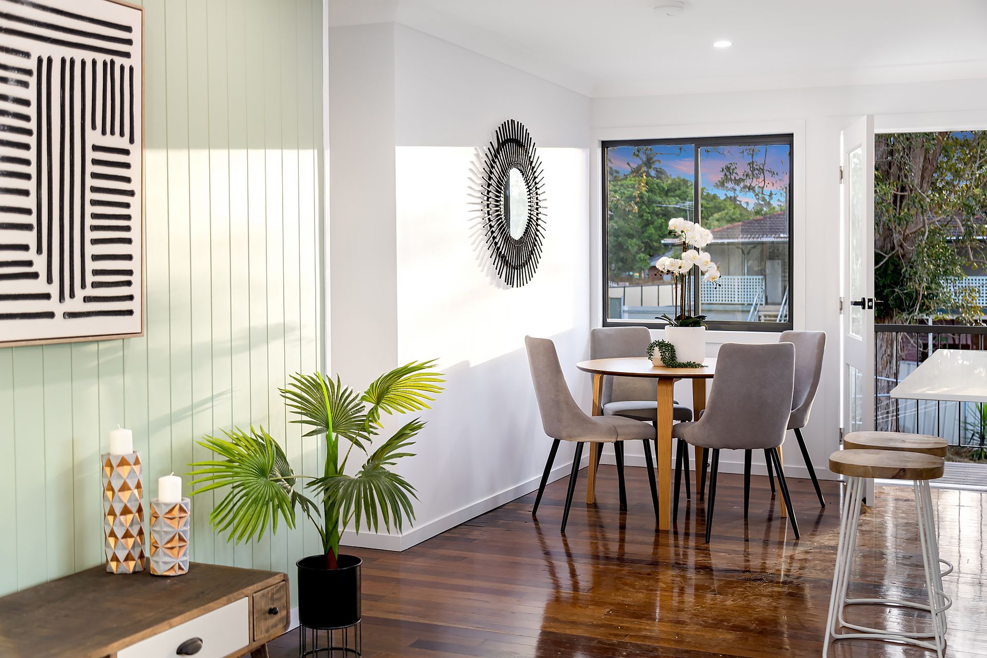 Dining room with table, chairs, and plant. Artwork on wall, hardwood floors.