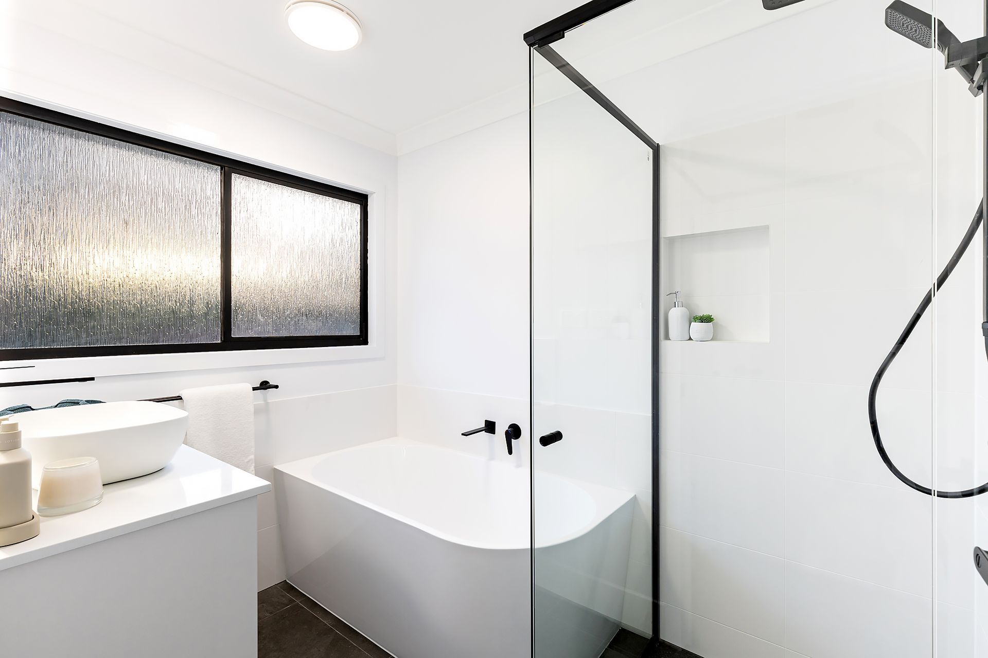 Modern white bathroom with a freestanding tub, glass shower, and black accents.