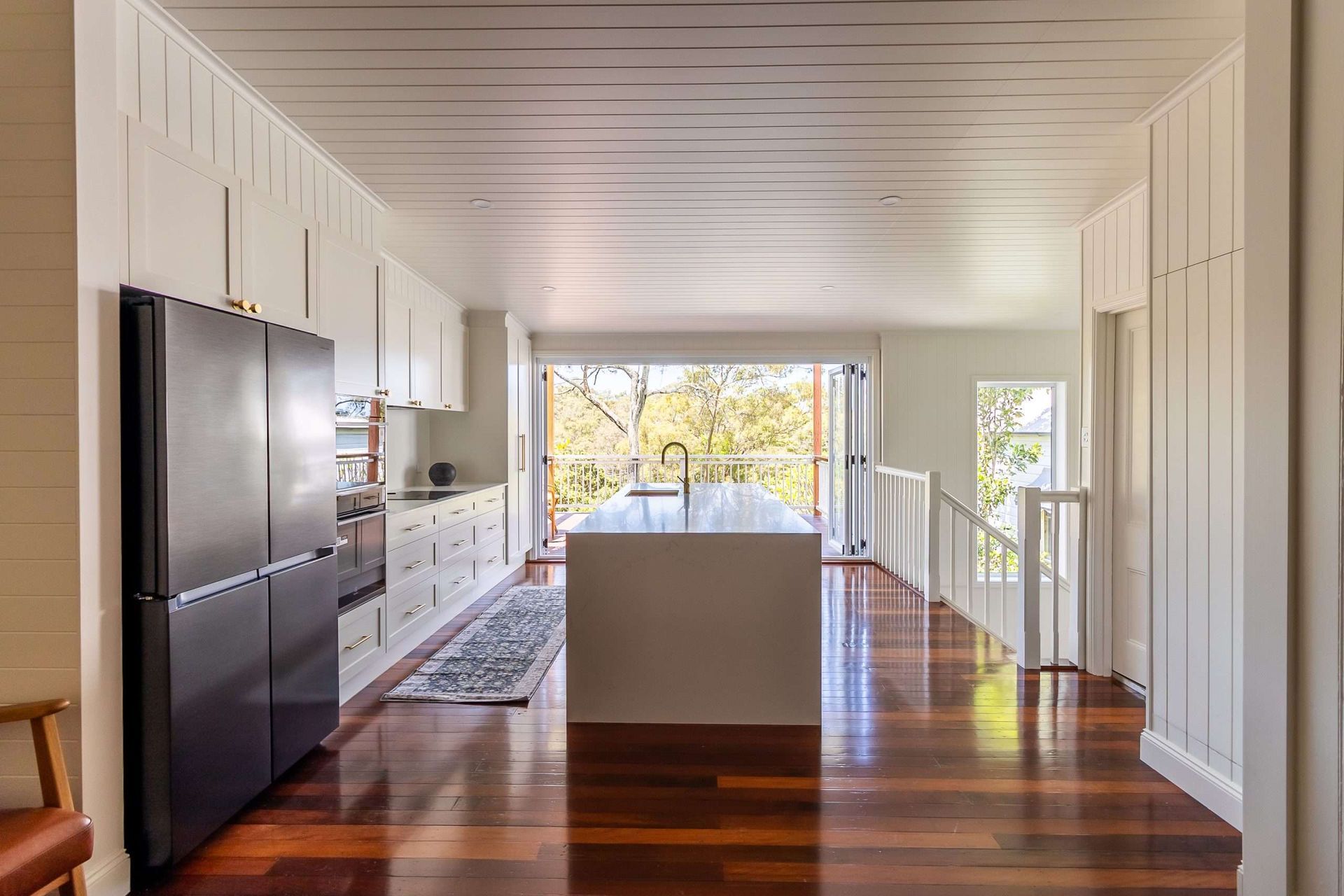 Kitchen with white cabinets, wood floor, black fridge, and island, leading to a balcony.