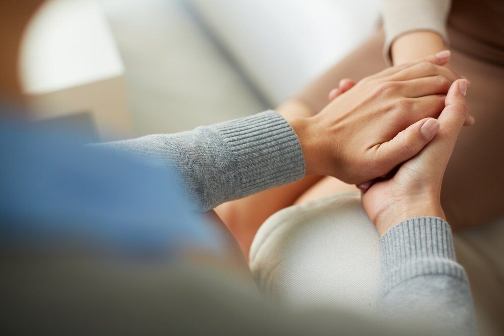 A Woman Is Holding Another Woman's Hand While Sitting On A Couch — The Red Chair Therapy in Blackwall, NSW