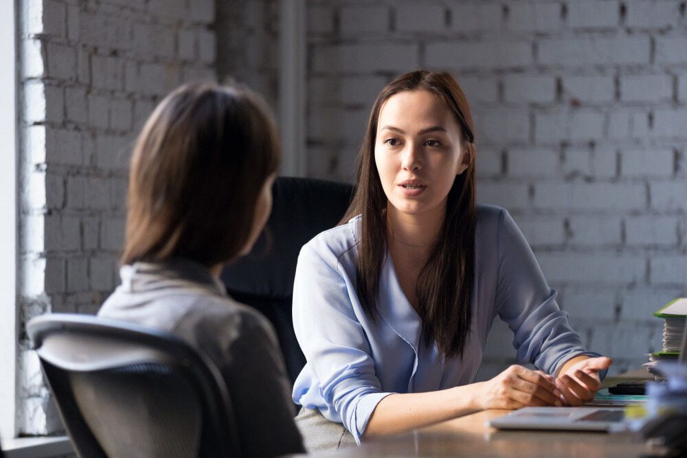 Two Women Are Sitting At A Table Having A Conversation — The Red Chair Therapy in Blackwall, NSW