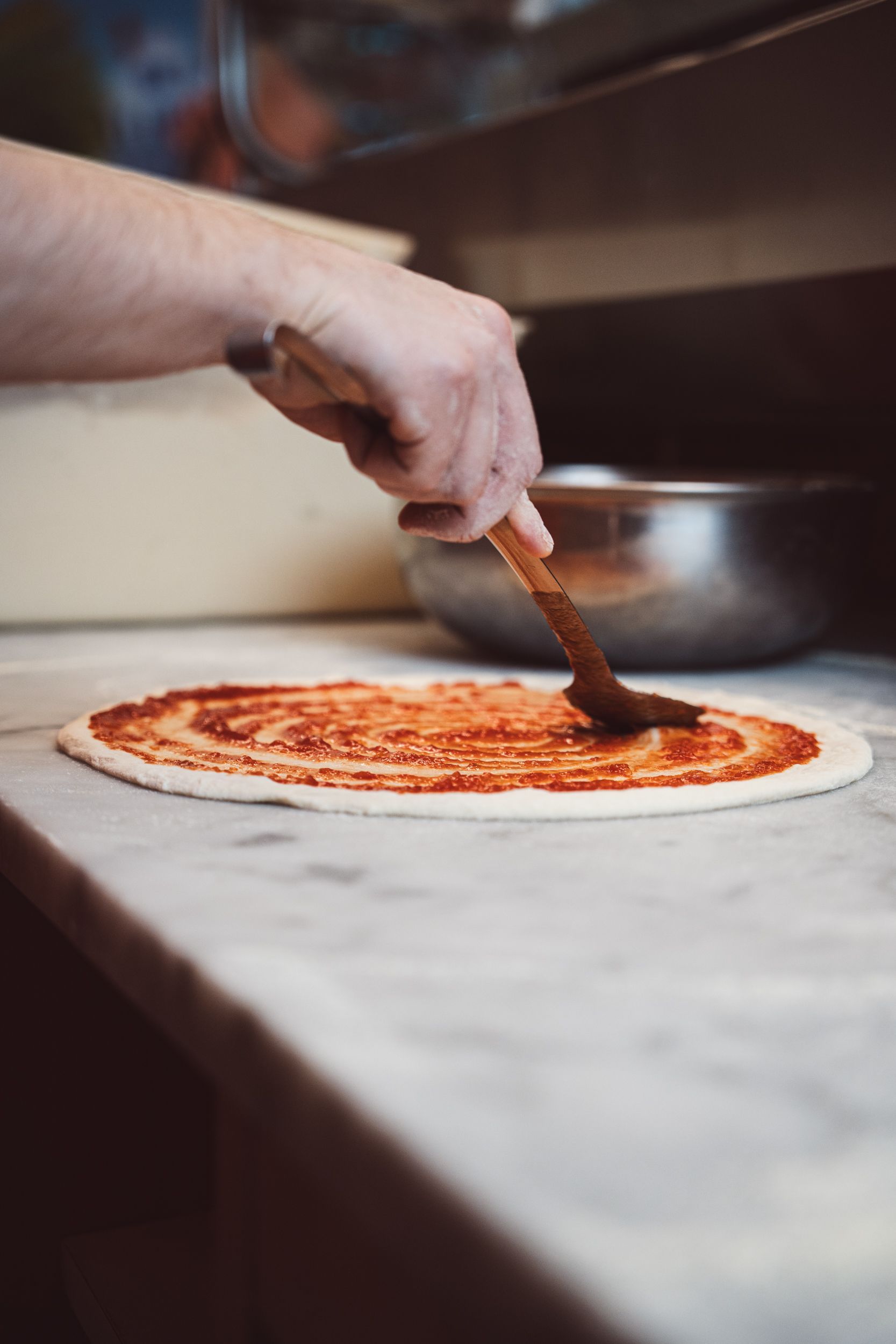 Una persona usa un cucchiaio di legno per spalmare la salsa di pomodoro rossa