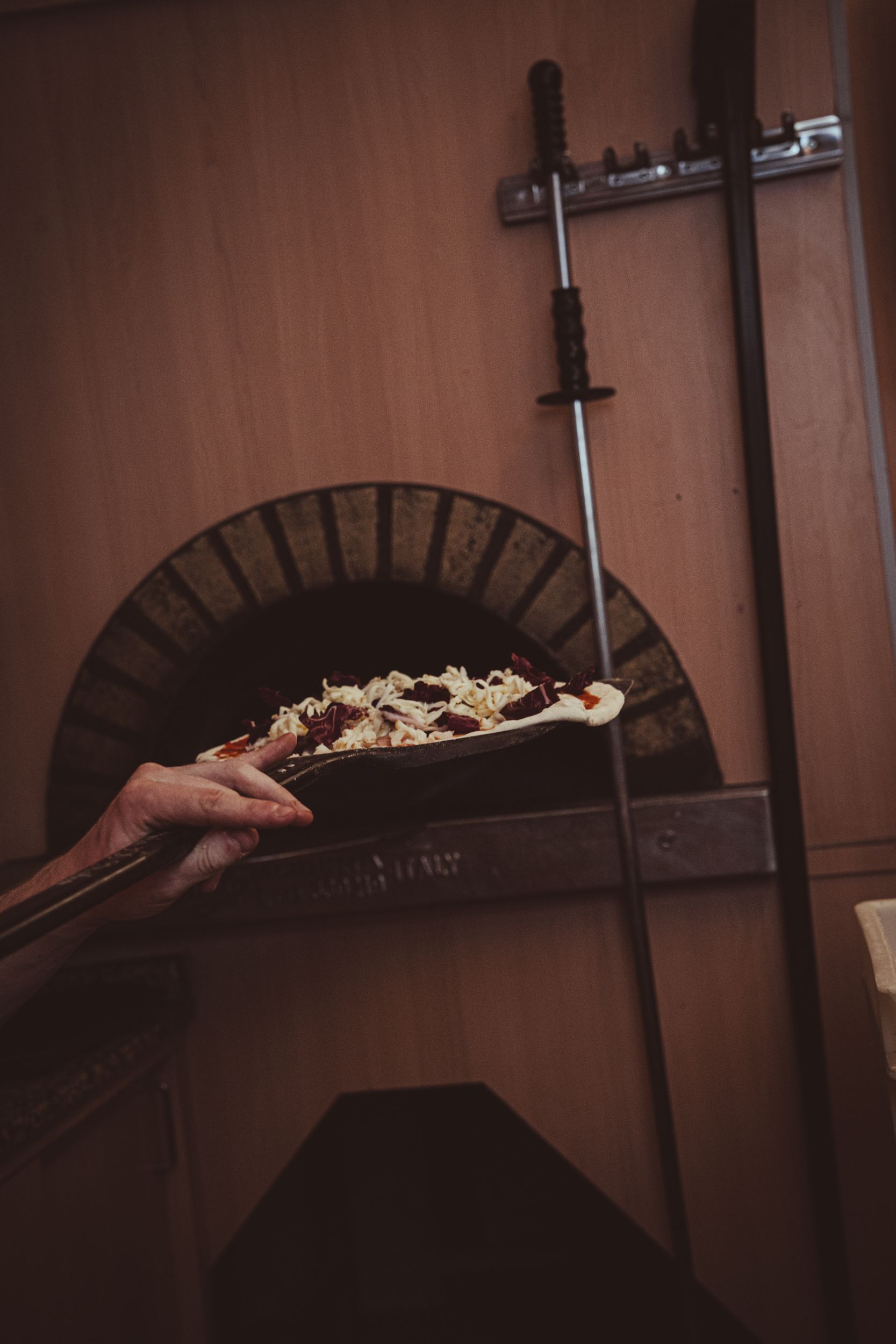 Una persona usa una pala per pizza per infornare una pizza farcita in un forno a legna in mattoni.