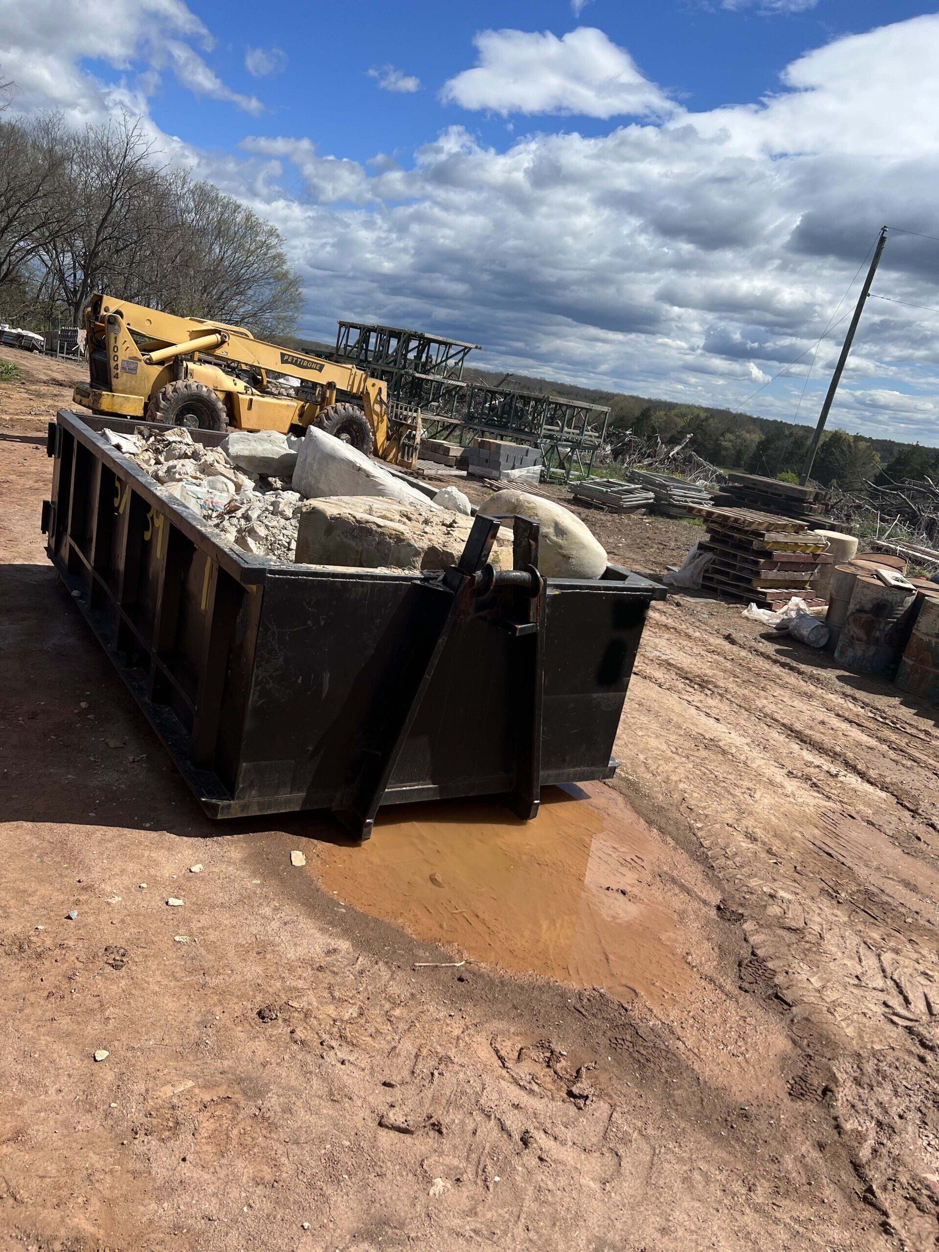 a dumpster filled with concrete and a bulldozer in the background .