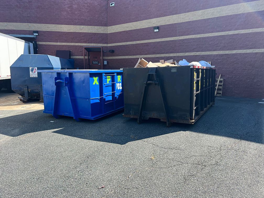 Two dumpsters are parked in front of a brick building.