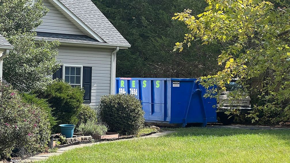 a white house with a blue dumpster in front of it .