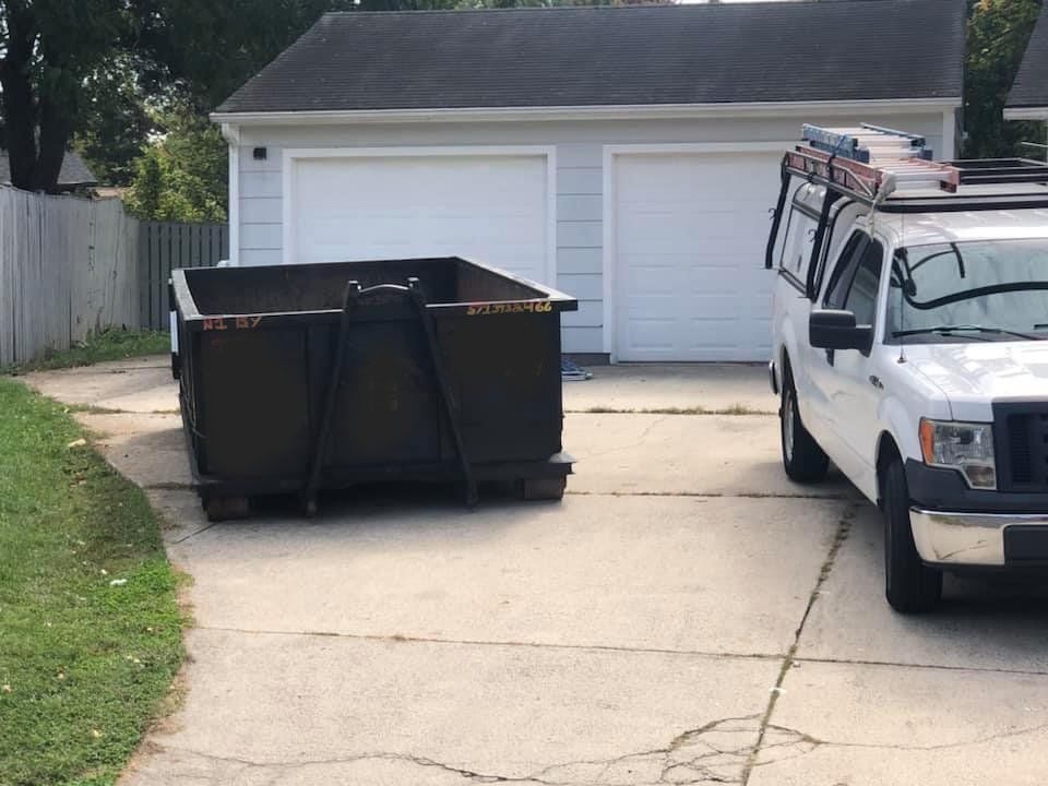 a dumpster and a truck are parked in a driveway in front of a garage .
