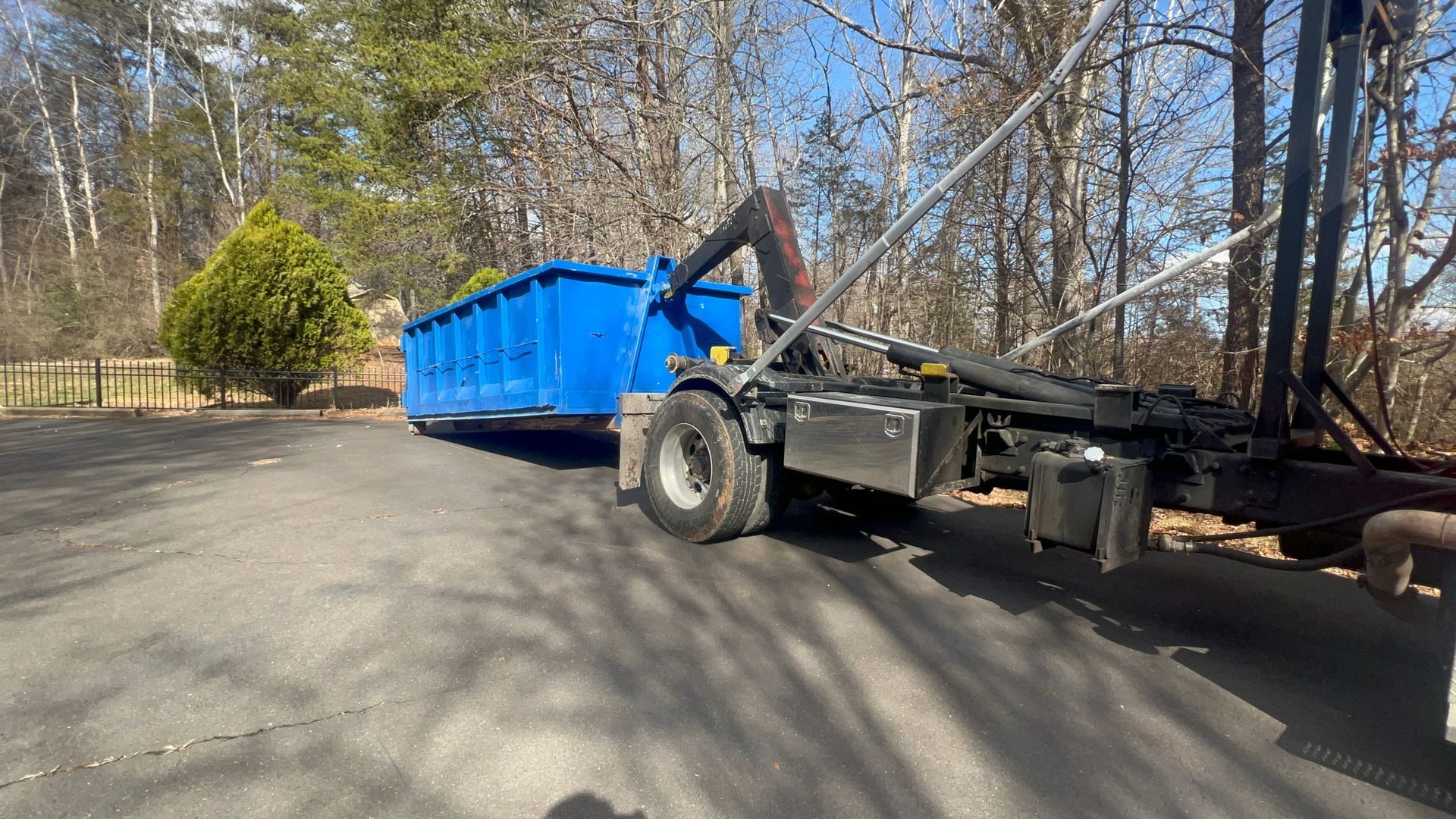 a blue dumpster is being pulled by a dump truck in a parking lot .